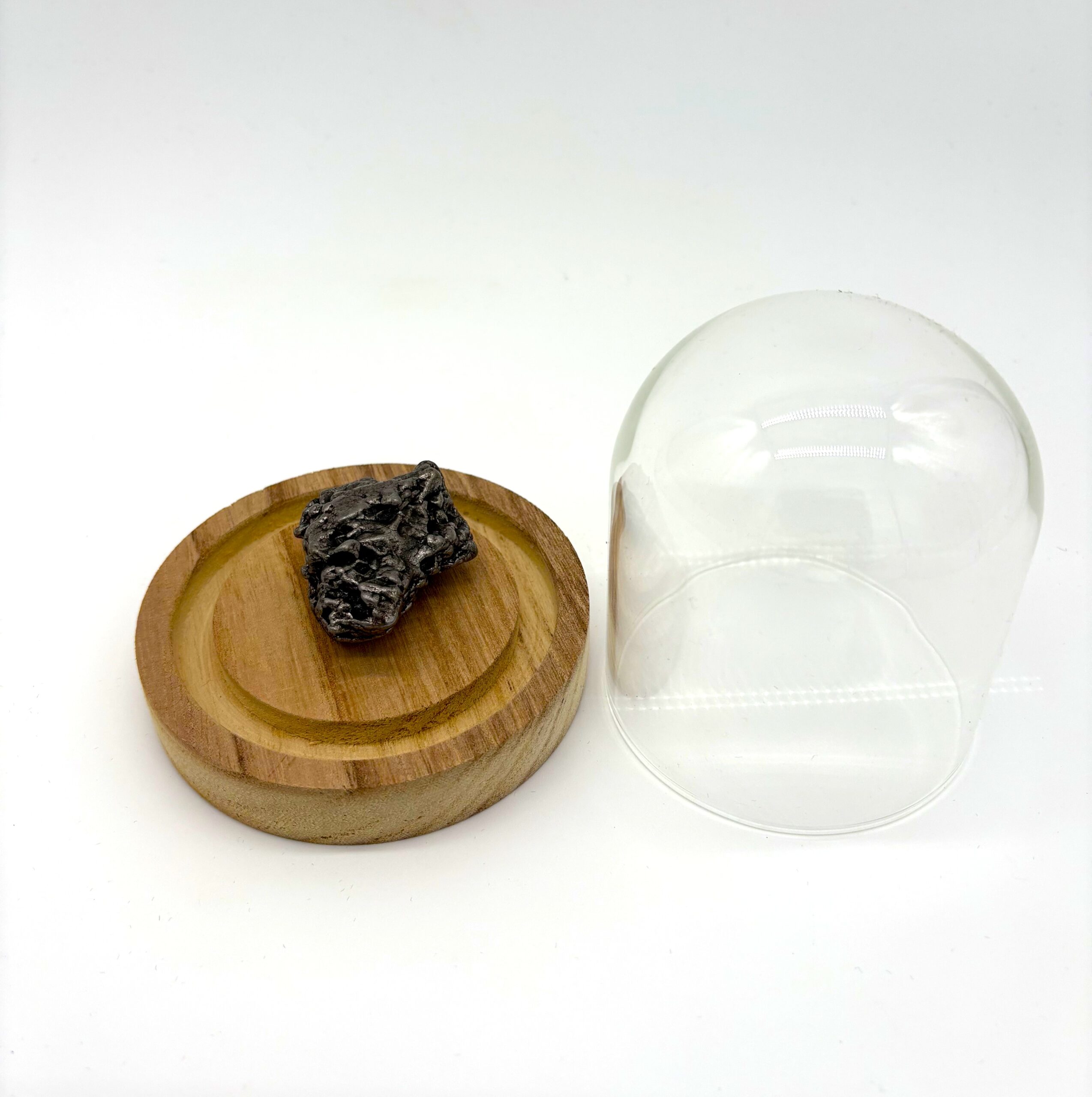 Medium-sized Campo del Cielo meteorite in glass cloche with light wood base.