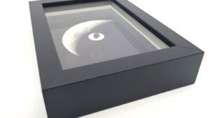 Black embossed frame containing a photograph of the Moon and a meteorite fragment