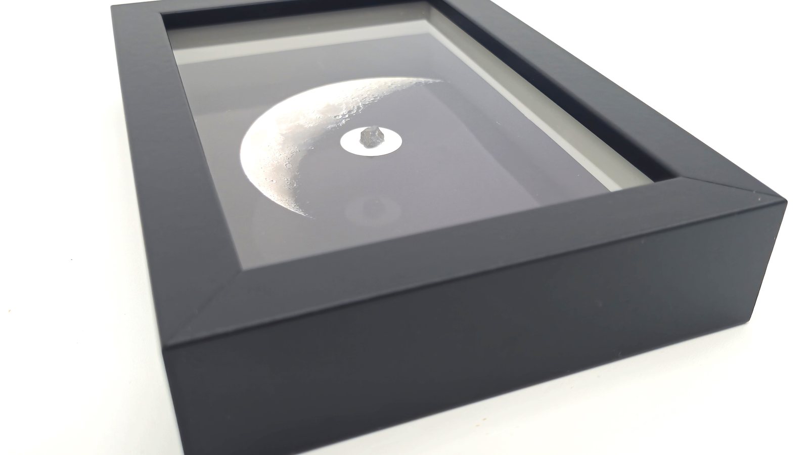 Black embossed frame containing a photograph of the Moon and a meteorite fragment